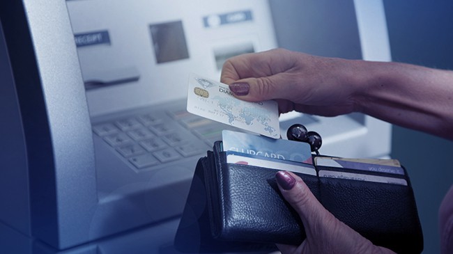 A woman removes her debit card from her wallet to use the ATM machine that is in front of her.