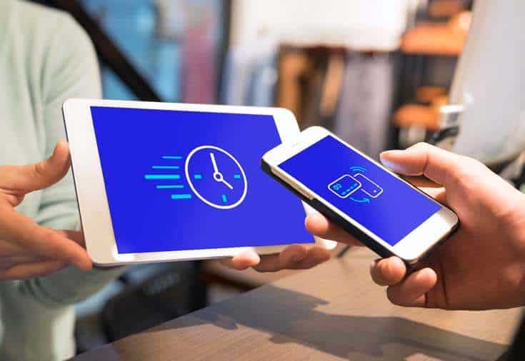 A person pays for their purchase by holding their smartphone to a tablet.