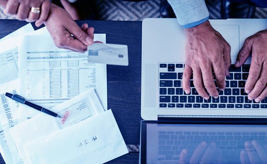 Photo of hands on a laptop keyboard and hands on papers