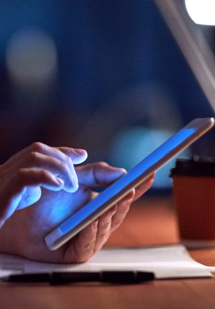Hands holding a tablet with blue light glowing from the screen onto the hands